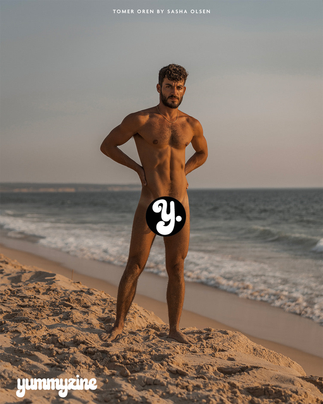 A naked man standing on a beach during sunset.
