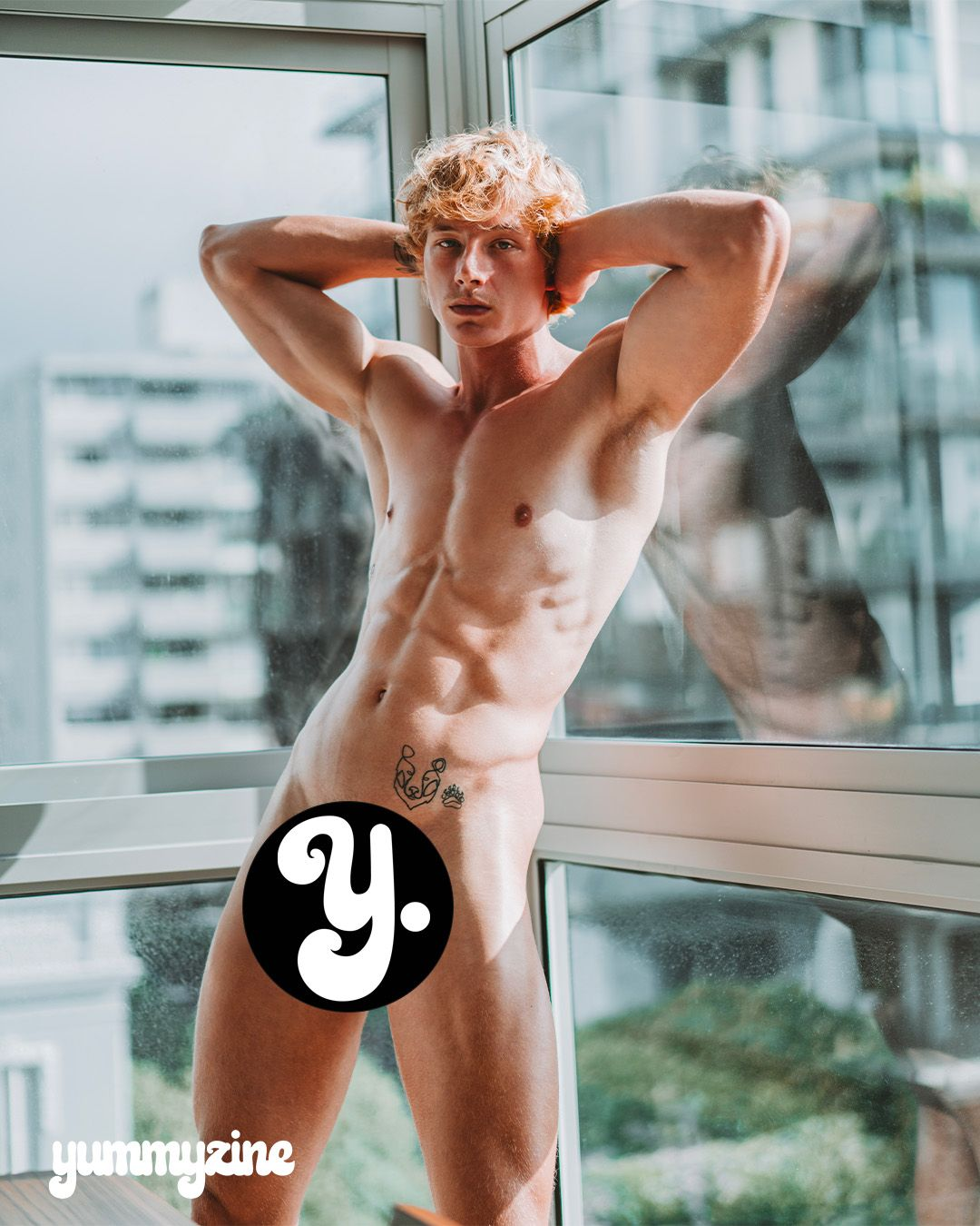 A muscular man posing by a window in a modern setting.