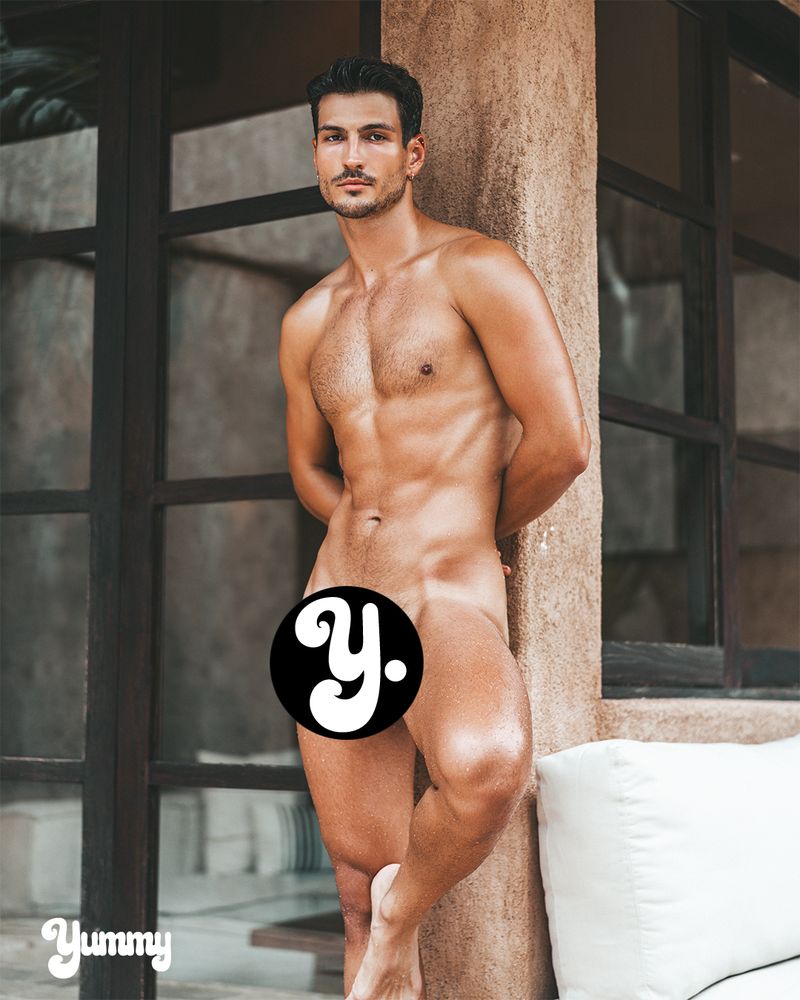 A muscular man posing in a natural setting, partially covered.