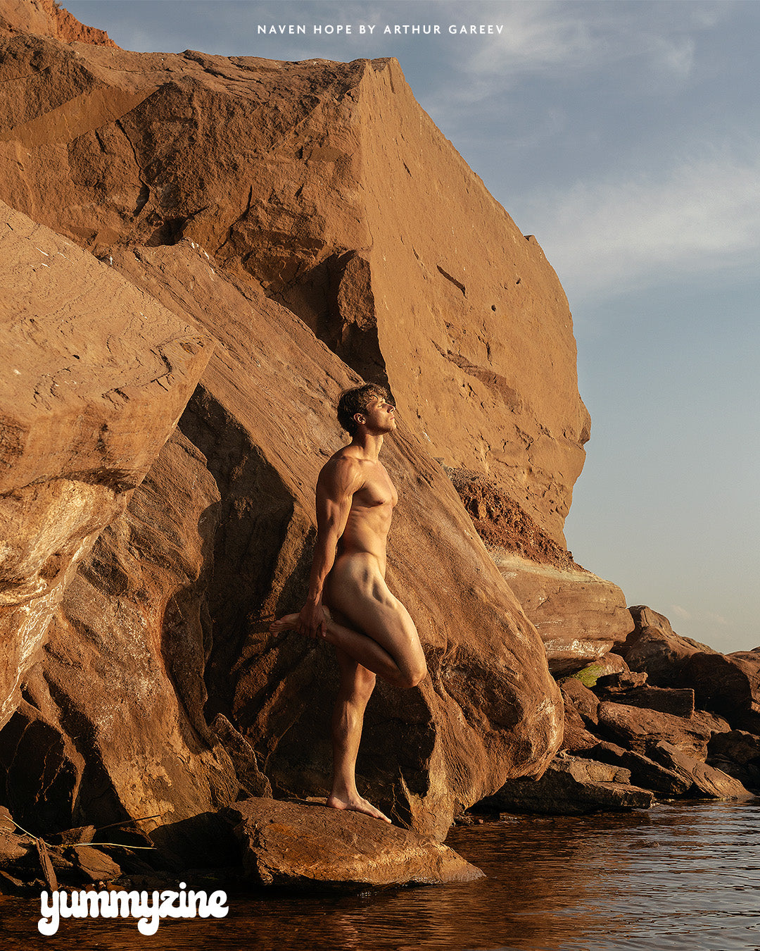 Person standing on a rock by water, with a natural landscape background.
